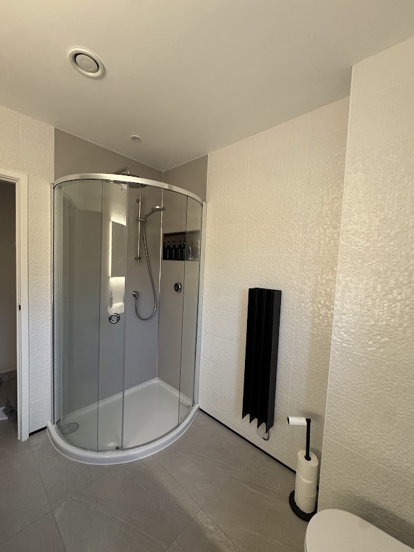 A quadrant shower enclosure with a black heated towel rail in a bright, textured-tile bathroom.
