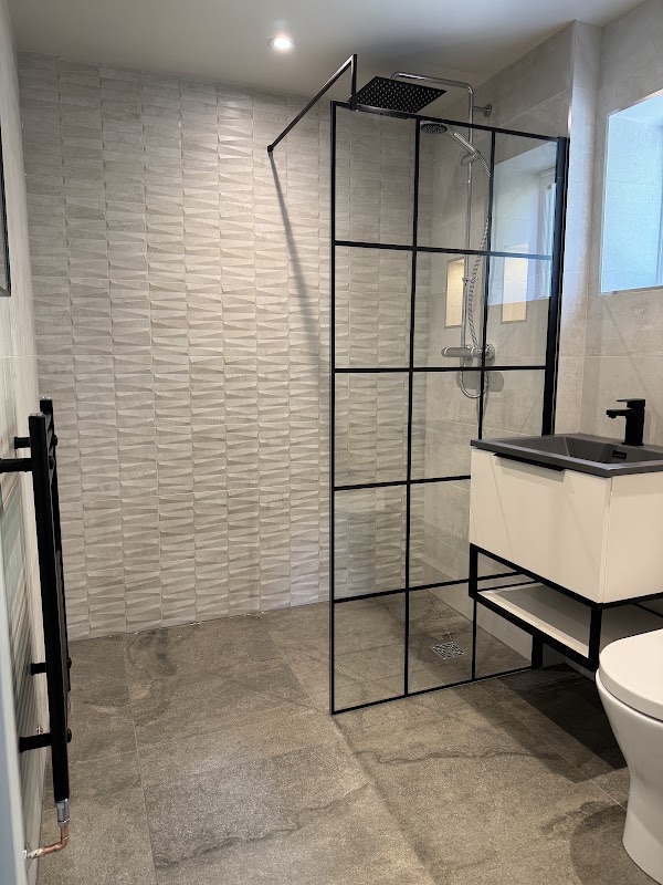 A walk-in shower with black framed screen, stone-effect tiling and a floating vanity.
